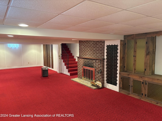 basement with a drop ceiling, carpet floors, and a brick fireplace