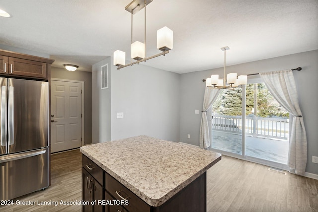 kitchen featuring hanging light fixtures, light hardwood / wood-style flooring, a kitchen island, stainless steel refrigerator, and a chandelier