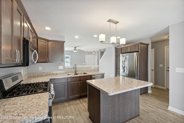 kitchen with sink, light wood-type flooring, appliances with stainless steel finishes, decorative light fixtures, and a kitchen island