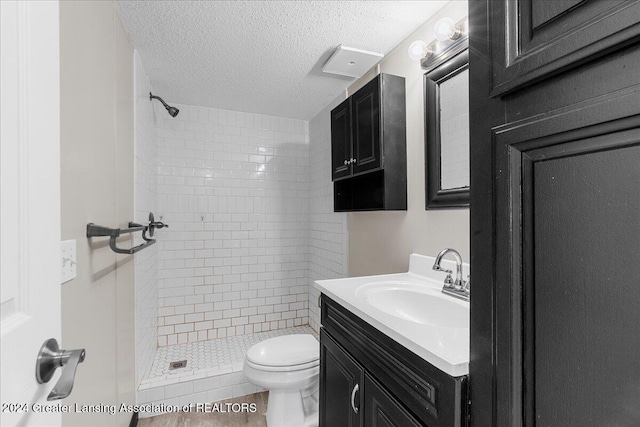 bathroom featuring a tile shower, vanity, a textured ceiling, and toilet