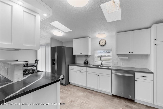 kitchen featuring a skylight, sink, stainless steel appliances, light hardwood / wood-style floors, and white cabinets