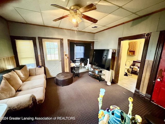 living room with ceiling fan, a drop ceiling, carpet floors, and ornamental molding