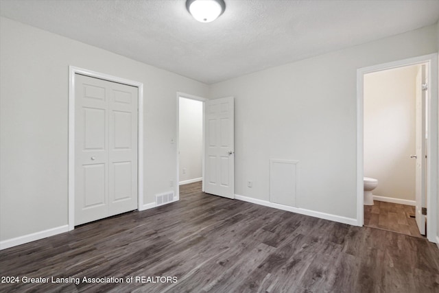 unfurnished bedroom with dark hardwood / wood-style floors, a textured ceiling, connected bathroom, and a closet