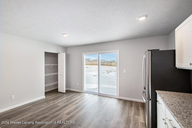 interior space with a textured ceiling, stainless steel fridge, white cabinetry, and dark hardwood / wood-style floors