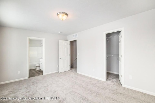 unfurnished bedroom with a walk in closet, ensuite bathroom, a closet, and carpet floors