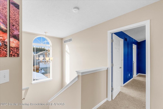 hall featuring a chandelier, light carpet, and a textured ceiling