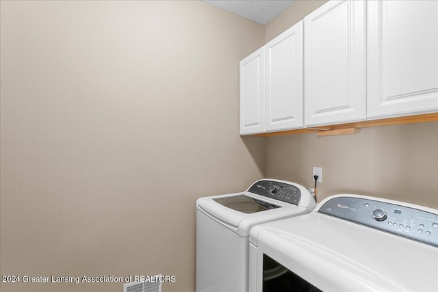 laundry room with washer and clothes dryer, cabinets, and a textured ceiling