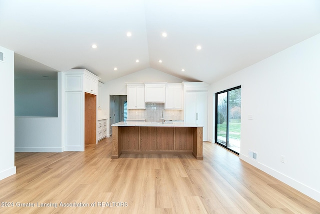 kitchen with white cabinets, lofted ceiling, a large island with sink, and light hardwood / wood-style flooring