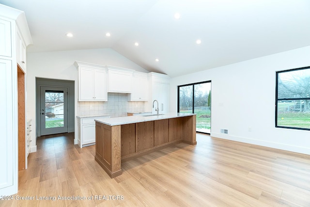 kitchen with sink, a large island with sink, light hardwood / wood-style flooring, white cabinets, and lofted ceiling