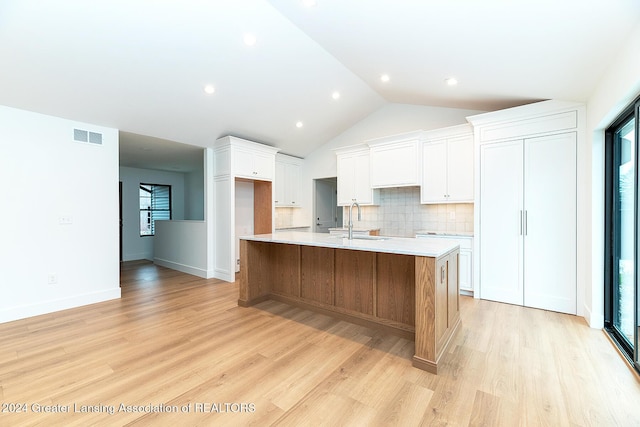 kitchen with white cabinets, light wood-type flooring, sink, and a large island with sink