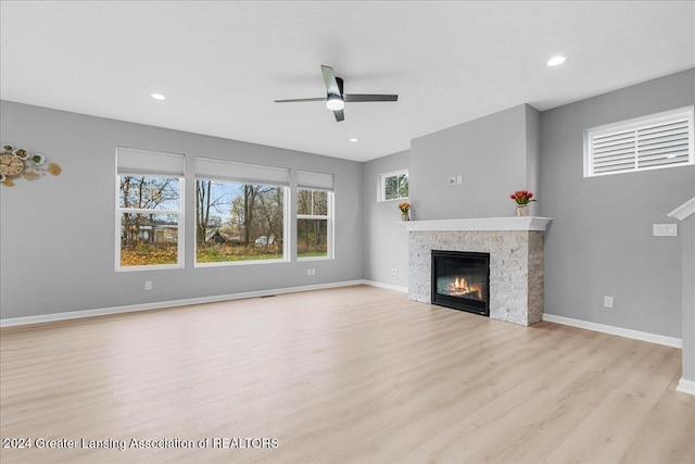 unfurnished living room with ceiling fan, a stone fireplace, and light hardwood / wood-style flooring