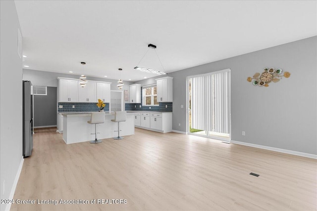 kitchen featuring a breakfast bar, a center island, white cabinets, hanging light fixtures, and light hardwood / wood-style flooring