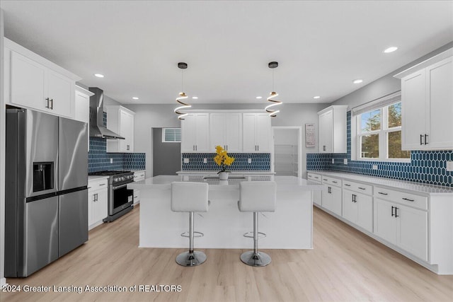 kitchen featuring appliances with stainless steel finishes, a center island, hanging light fixtures, and wall chimney exhaust hood