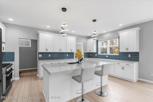 kitchen featuring light wood-type flooring, white cabinetry, hanging light fixtures, and high end stainless steel range