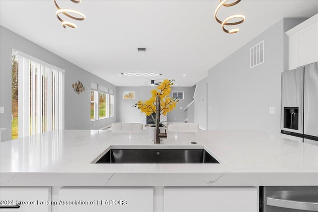 kitchen featuring stainless steel fridge, light stone counters, sink, an inviting chandelier, and white cabinets