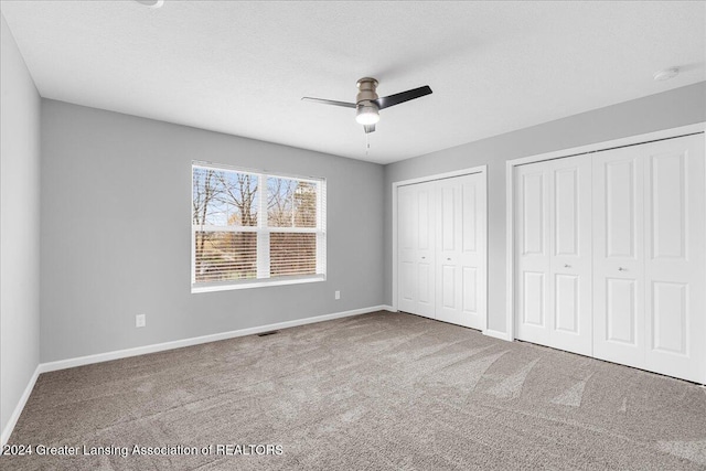 unfurnished bedroom with two closets, a textured ceiling, light colored carpet, and ceiling fan