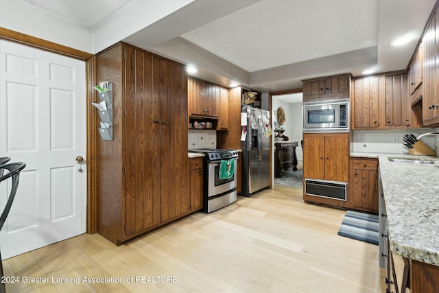 kitchen with sink, stainless steel appliances, tasteful backsplash, and light hardwood / wood-style flooring