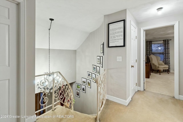 hallway with light carpet, lofted ceiling, and a notable chandelier