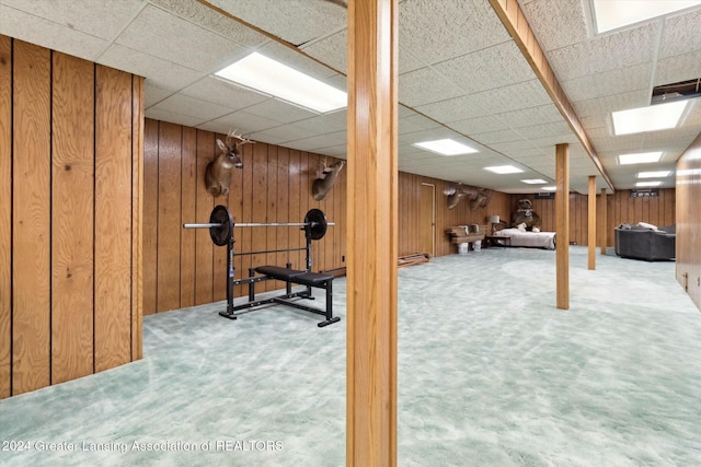 basement featuring carpet flooring, a drop ceiling, and wooden walls