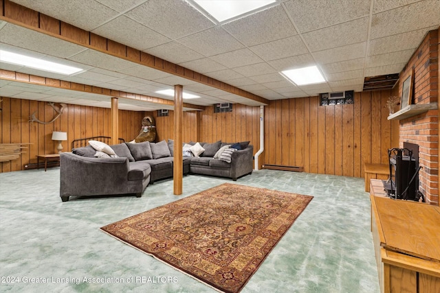 carpeted living room featuring a drop ceiling, a fireplace, baseboard heating, and wooden walls