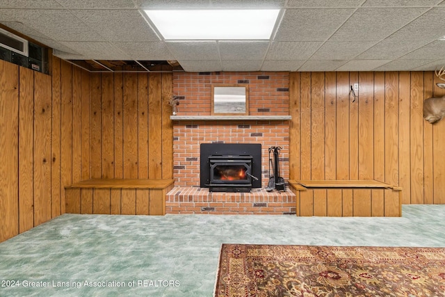 carpeted living room featuring a paneled ceiling, wood walls, and a wood stove