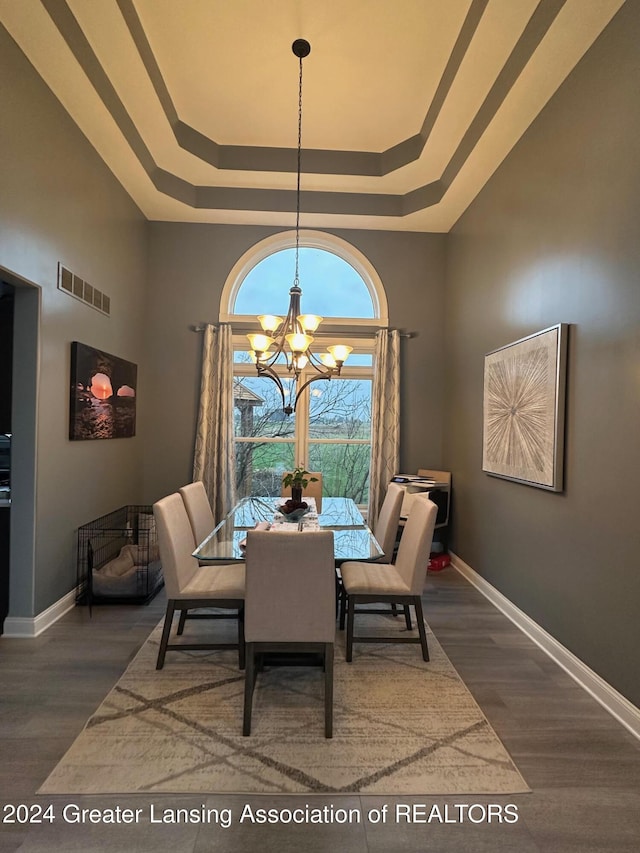 dining space with a raised ceiling, dark wood-type flooring, and a notable chandelier