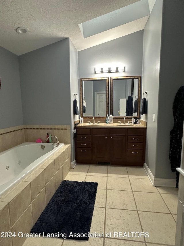 bathroom featuring vanity, tile patterned floors, vaulted ceiling with skylight, a textured ceiling, and tiled bath