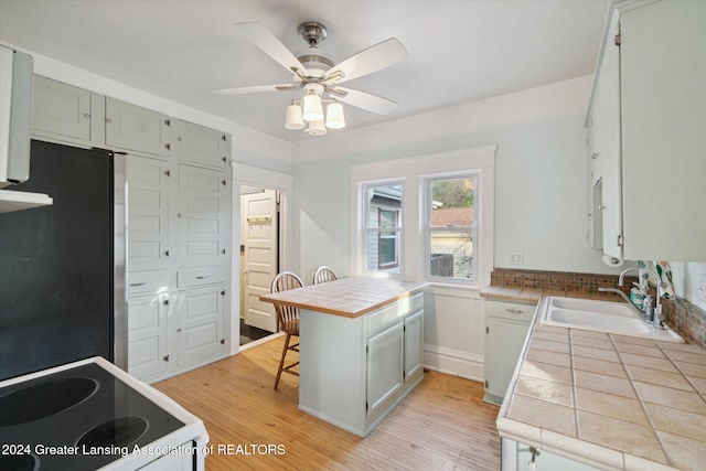 kitchen with light wood-type flooring, sink, tile countertops, range, and stainless steel refrigerator