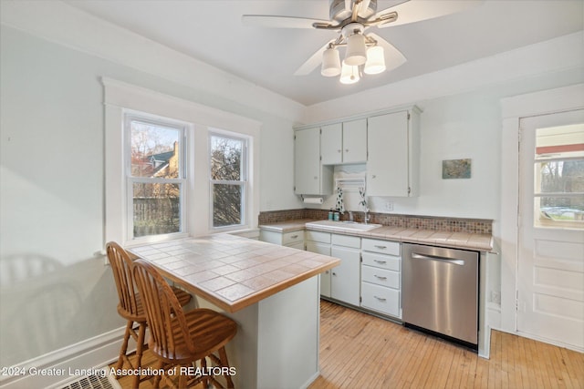 kitchen featuring sink, stainless steel dishwasher, ceiling fan, tile counters, and light hardwood / wood-style floors