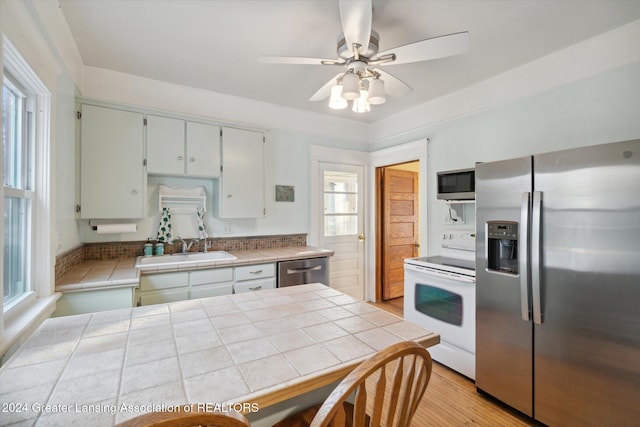 kitchen featuring ceiling fan, sink, tile countertops, light hardwood / wood-style floors, and appliances with stainless steel finishes