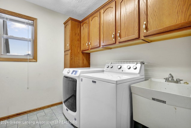 clothes washing area featuring sink, cabinets, washing machine and dryer, a textured ceiling, and light tile patterned floors