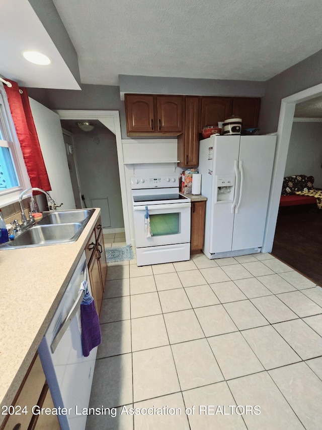 kitchen with light tile patterned flooring, a textured ceiling, white appliances, and sink