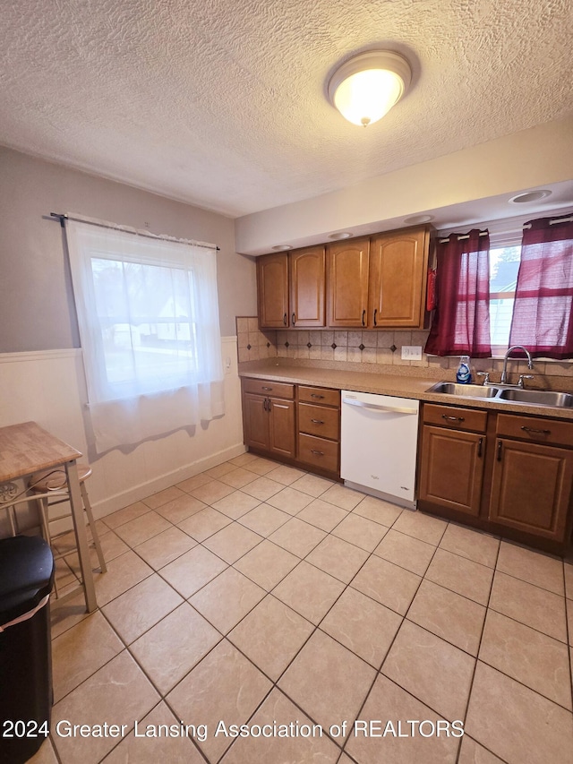 kitchen with dishwasher, light tile patterned floors, a textured ceiling, and sink