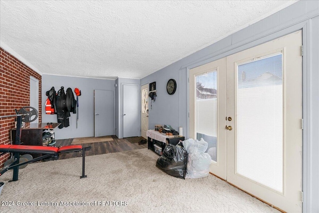 exercise area with carpet, a textured ceiling, brick wall, and french doors