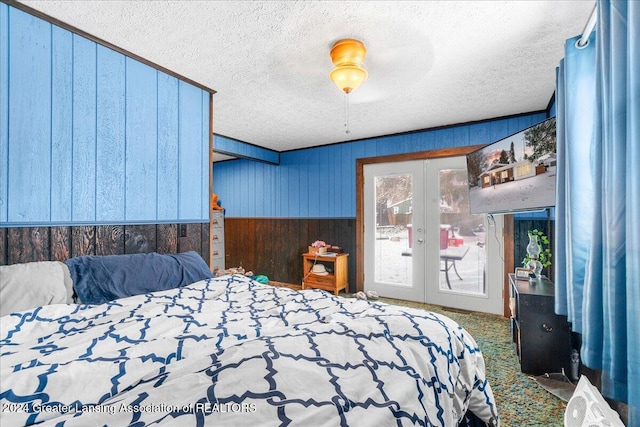 carpeted bedroom with a textured ceiling, ceiling fan, french doors, and wood walls