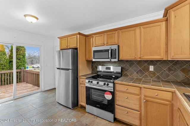 kitchen featuring appliances with stainless steel finishes, tile countertops, tasteful backsplash, and crown molding