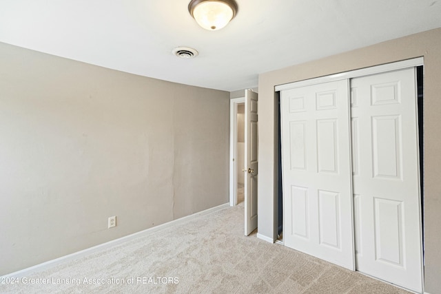 unfurnished bedroom with light colored carpet and a closet