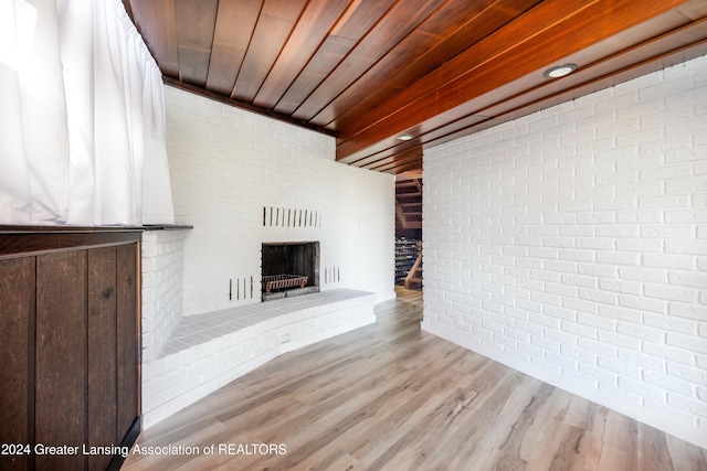 unfurnished living room with light hardwood / wood-style floors, wooden ceiling, brick wall, and a brick fireplace