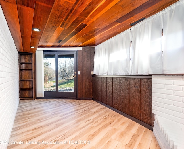 spare room featuring brick wall, light hardwood / wood-style floors, wood walls, and wood ceiling