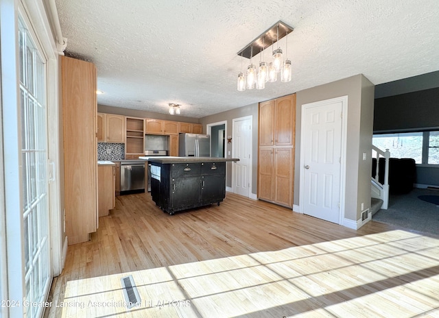 kitchen featuring a center island, decorative light fixtures, decorative backsplash, appliances with stainless steel finishes, and light wood-type flooring