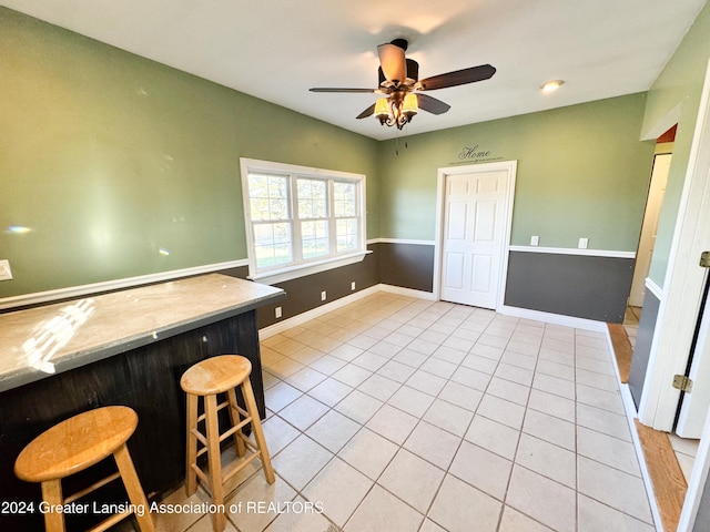 interior space with a breakfast bar, ceiling fan, and light tile patterned floors