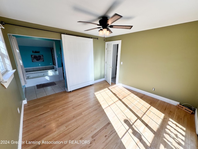 unfurnished bedroom with light wood-type flooring, ensuite bathroom, and ceiling fan