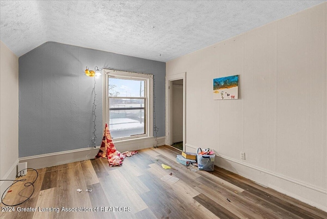 empty room featuring hardwood / wood-style floors, lofted ceiling, and a textured ceiling