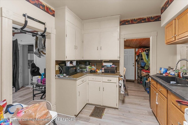 kitchen with white cabinets, tasteful backsplash, sink, and light hardwood / wood-style flooring