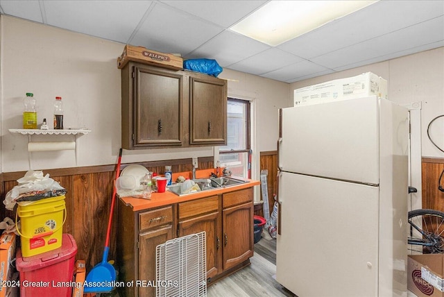 kitchen with a drop ceiling, wood walls, sink, light hardwood / wood-style floors, and white fridge