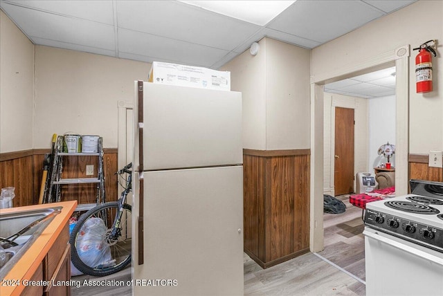 kitchen featuring light wood-type flooring, a paneled ceiling, white appliances, wooden walls, and sink