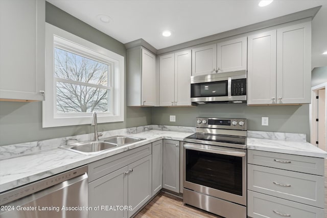 kitchen with sink, light stone counters, light hardwood / wood-style floors, gray cabinets, and appliances with stainless steel finishes