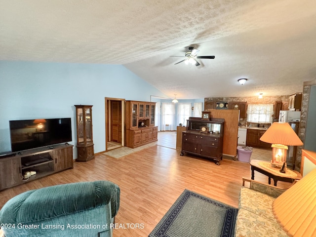 living room with vaulted ceiling, ceiling fan, light hardwood / wood-style floors, and a textured ceiling