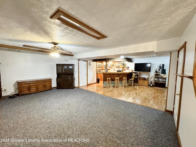 living room with bar, ceiling fan, light hardwood / wood-style floors, and a textured ceiling