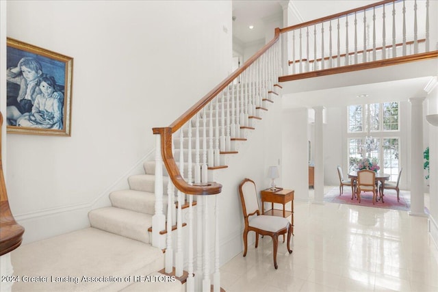 staircase featuring tile patterned flooring, a towering ceiling, and decorative columns